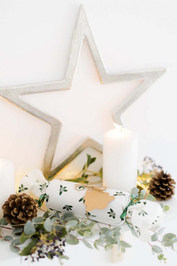 A Christmas scene featuring a silver star, lit candle and fabric reusable crackers