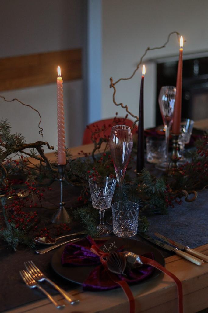Velvet napkins sit on top of a black plate. Subtle candle light from coloured candlesticks amongst forged greenery.